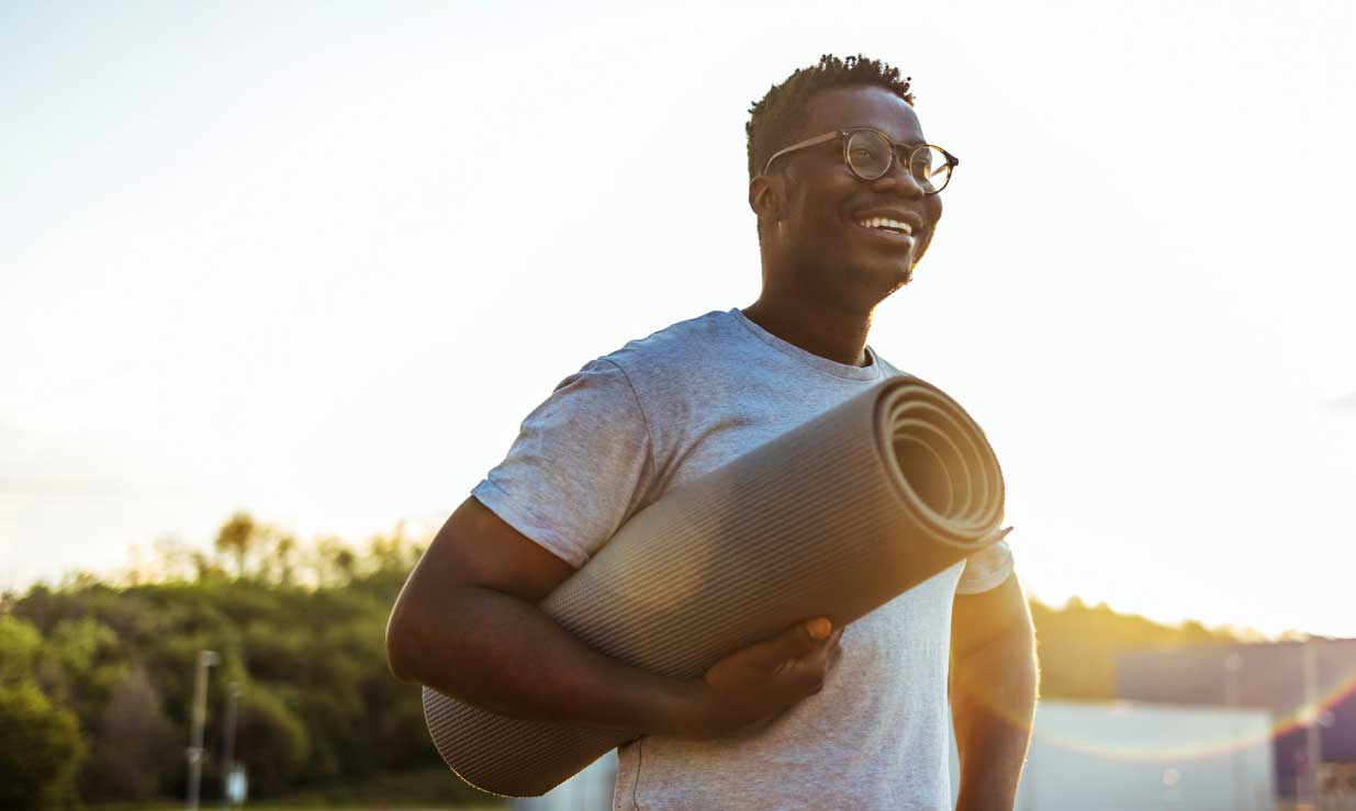 bnr-blue365 Man with glasses smiling and holding a yoga mat under his arm